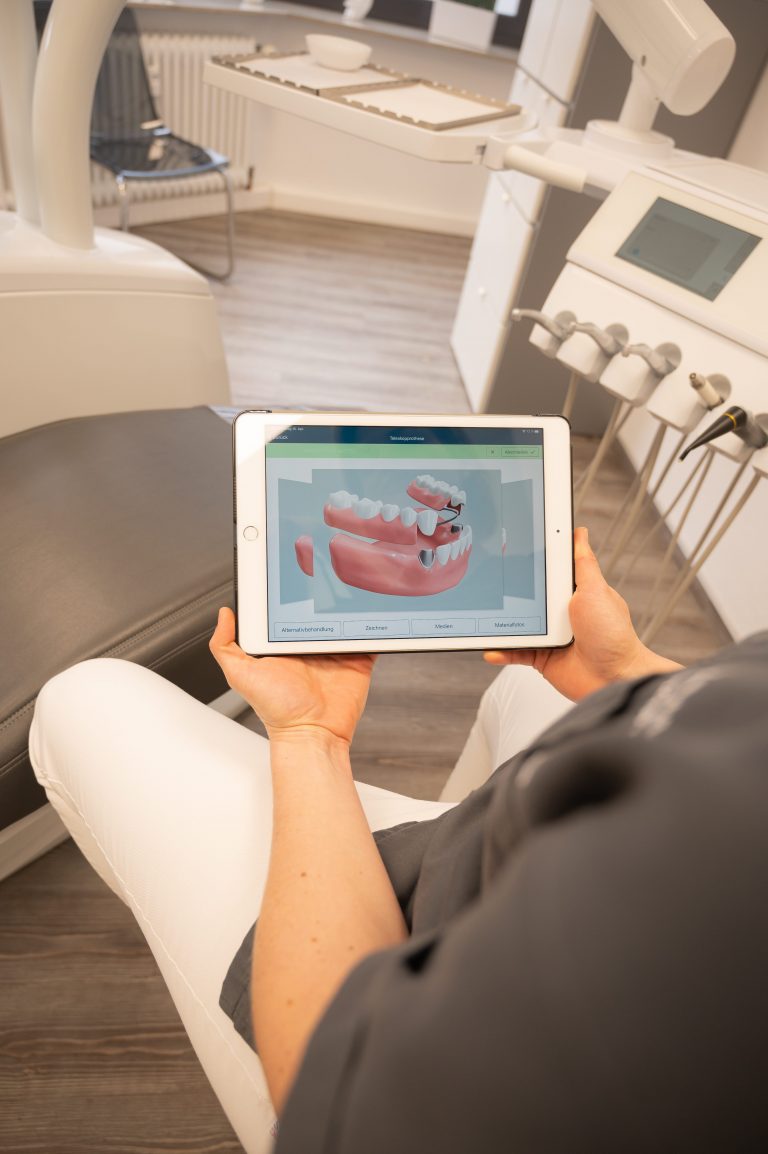 zahnaerztin sitzt im Behandlungsraum und haelt tablet in der hand welches neueste Kiefer und Zahntechnik zeigt