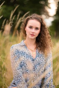 blonde Frau mit Naturlocken sitzt mit blauem Bluemchen Kleid auf wiese, harmonische und natuerliche farben