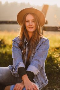 junge Frau sitzt in Natur und traegt Jeansjacke und Cowboyhut - natuerliches portrait