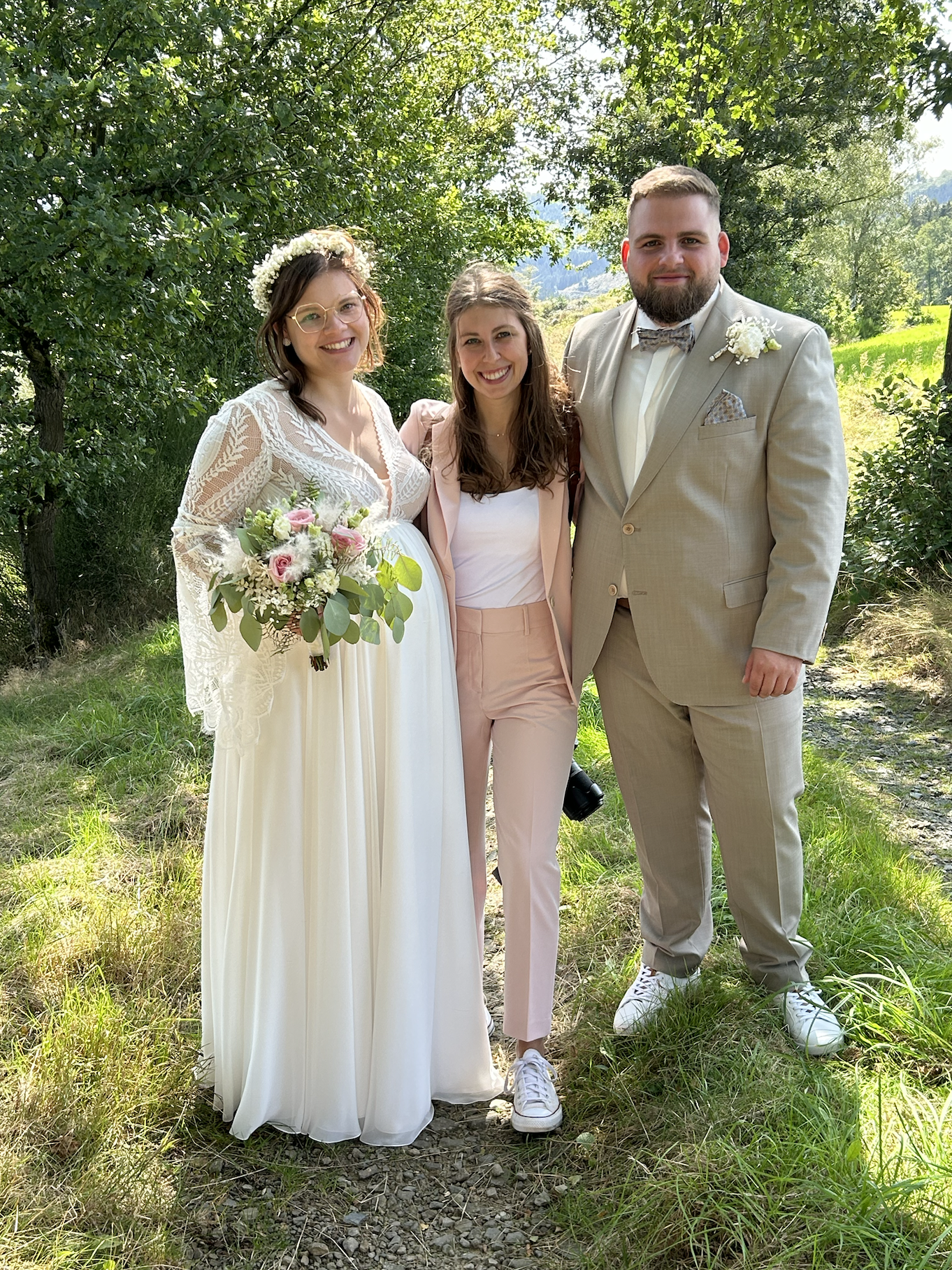 Hochzeitsfotografin Arm in Arm mit gluecklichem Brautpaar auf einer Wiese bei Sonnenschein nach fertigen Brautpaarfotos