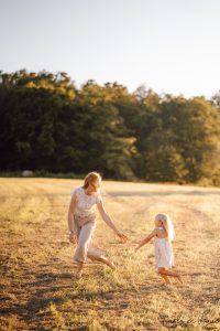 kleines maedchen spielt mit mama barfuß auf wiese fangen bei sonnenschein