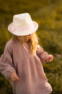 Natuerliches Portrait von Maedchen mit rosa Kleid und weißem Hut sammelt auf Wiese Blumen