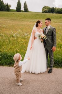 Brautpaar lachelt sich an und Sohn kommt mit Blume