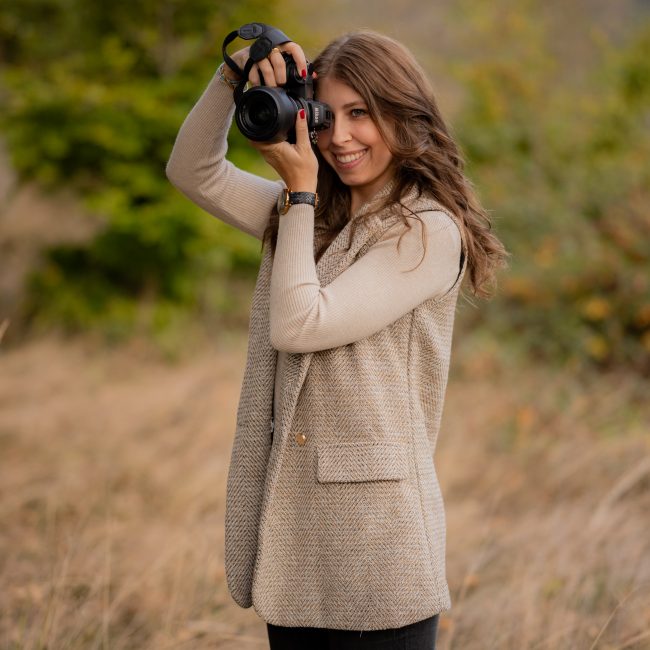 Fotografin steht in Natur und fotografiert selbstportrait