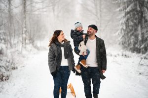 Familienfoto von lächelnden Mama Papa und Sohn mit Schlitten im verschneiten Wald