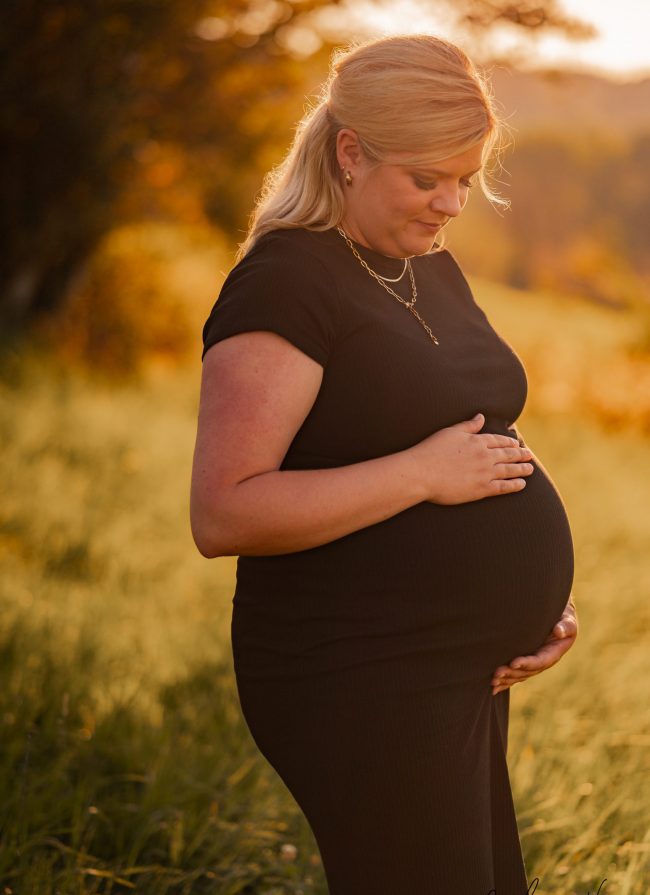 schwangere Frau steht auf wiese und blickt auf Babybauch