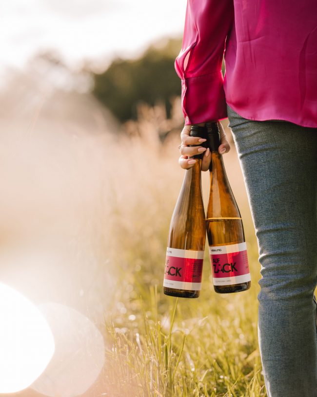 Produktportrait von Frau mit pinker bluse, die ihren wein "auf zack" von weinhaftig in der hand haelt, als Produktvermarktung