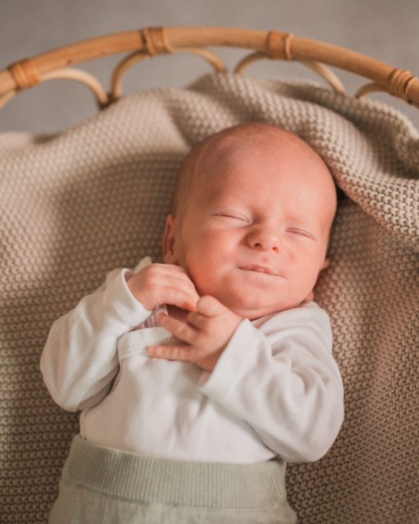 2 Wochen altes Baby liegt auf einer beigen Decke in einem geflochtenen Korb für ein babyfoto