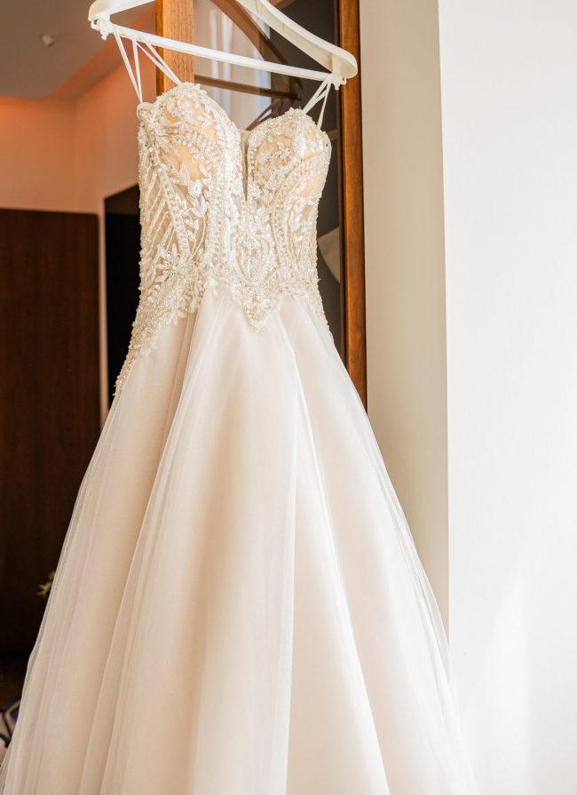 Weißes Brautkleid mit Perlenverzierung haengt am Schrank