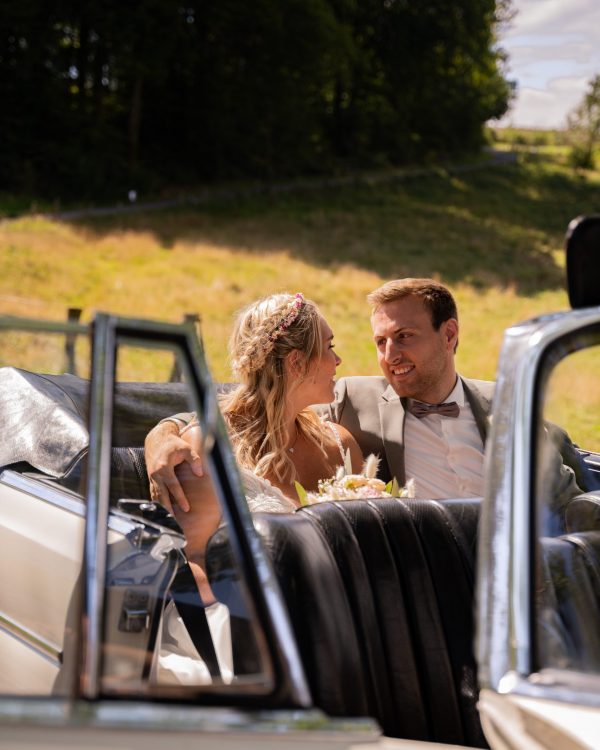 Hochzeitsfoto von braut im arm von Bräutigam in beigem Cabrio bei sonnenschein