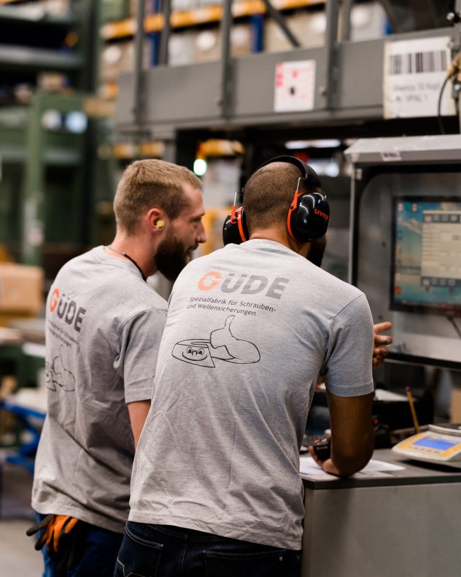 zwei mitarbeiter mir Unternehmenskleidung stehen vor computer und besprechen den produktionsprozess