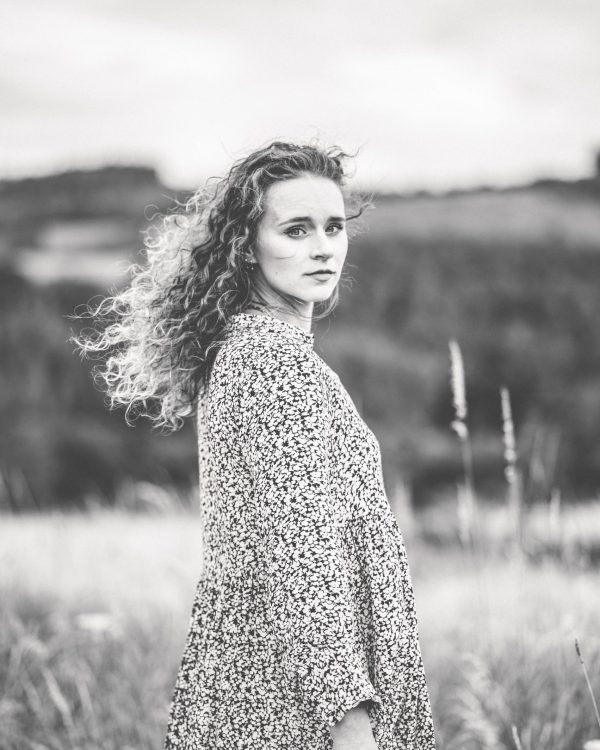 portrait-von-frau-mit-wilden-naturlocken-traegt-kleid-auf-wiese